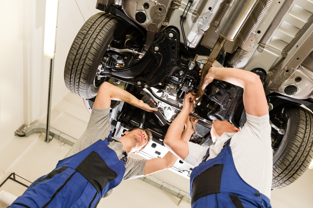Two mechanics repair a raised car in an auto shop