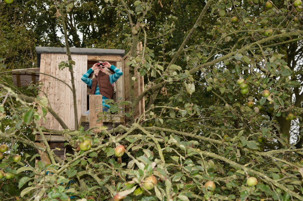 A girl in a treehouse while using a binoculars to inspect the surroundings